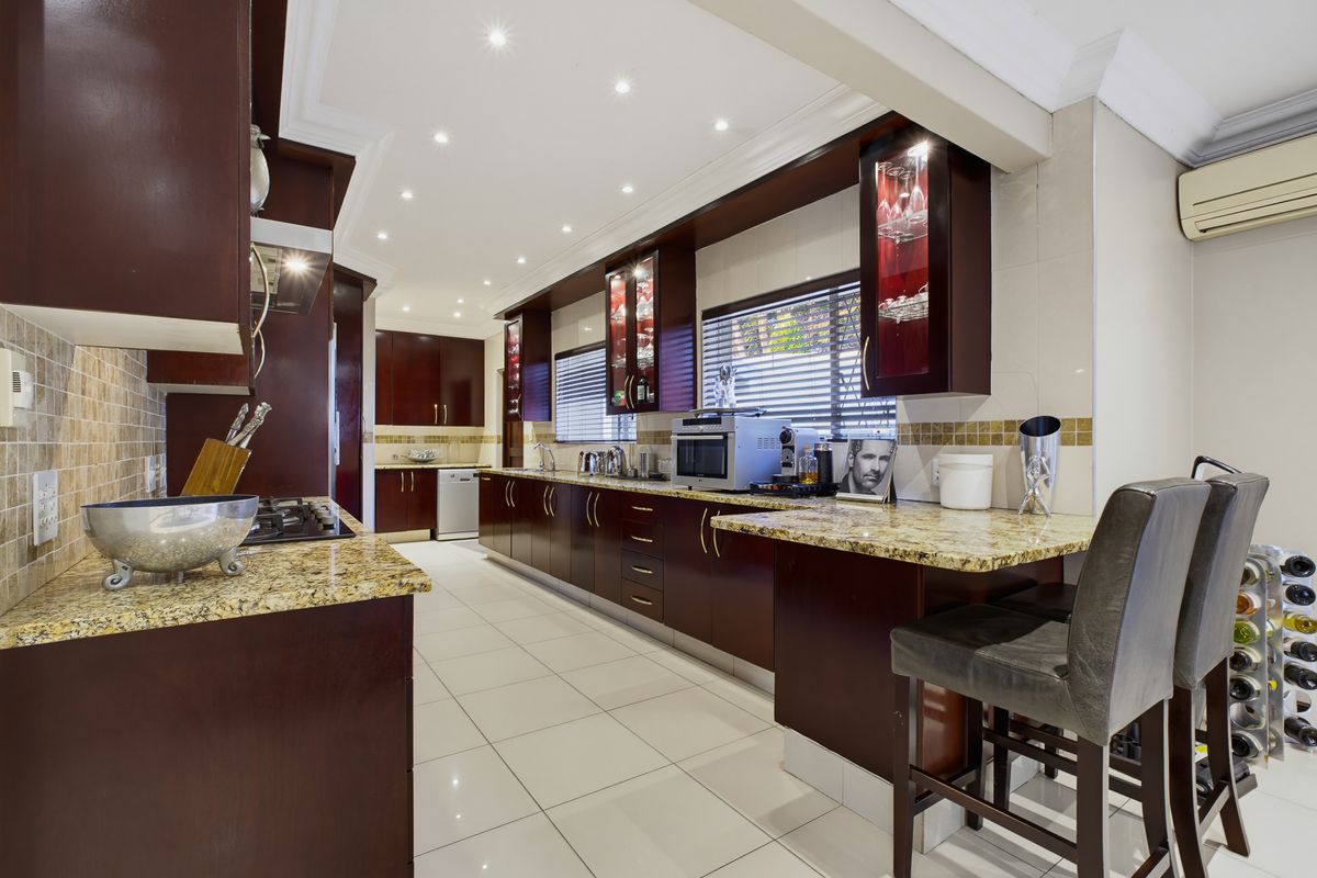 Spacious kitchen featuring dark wood cabinetry, granite countertops, mosaic tile backsplash, and integrated appliances with a breakfast bar area.
