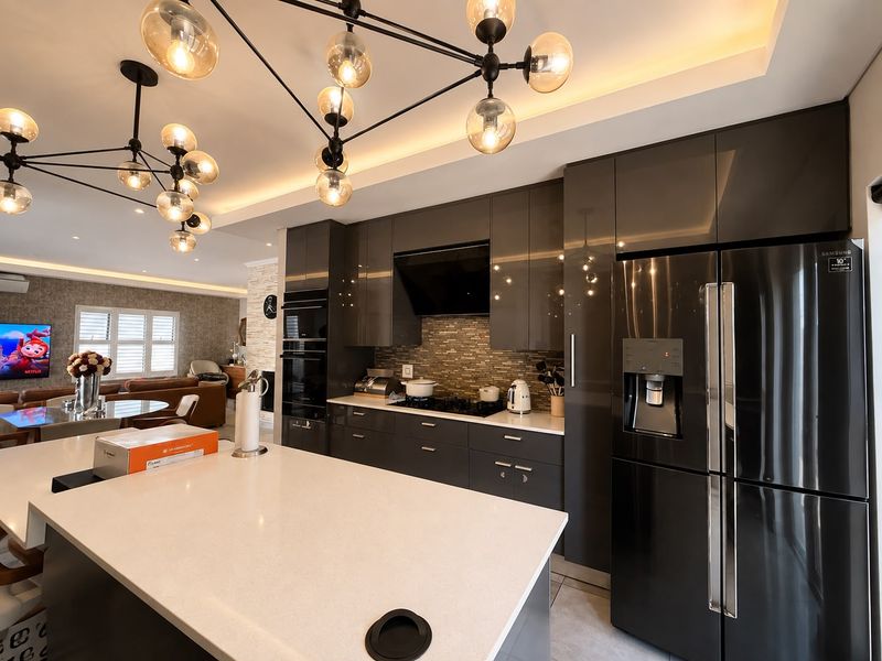 Modern open-plan kitchen featuring high-gloss cabinetry, quartz countertops, a central island, and integrated appliances, seamlessly flowing into the living area.