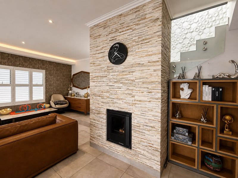 A modern living room featuring a prominent stone-clad fireplace, recessed lighting, and a stylish glass staircase with a textured feature wall.