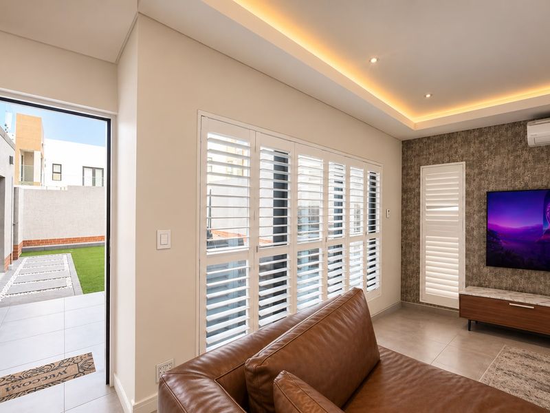 Modern living room featuring recessed cove lighting, plantation shutters, tiled floors, and a feature wall with an integrated air conditioning unit.
