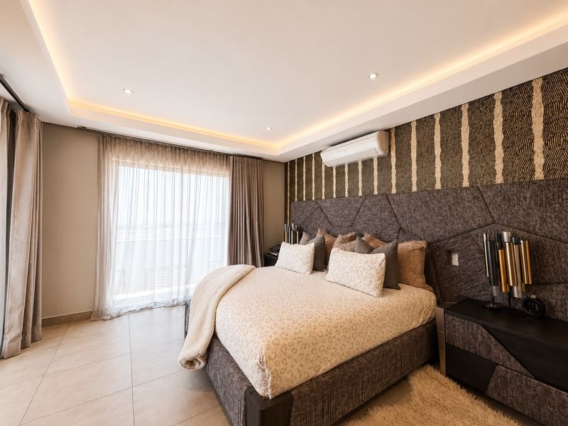 Modern bedroom featuring tiled flooring, recessed cove lighting, a split-system air conditioner, and a large sliding glass door leading to a balcony.