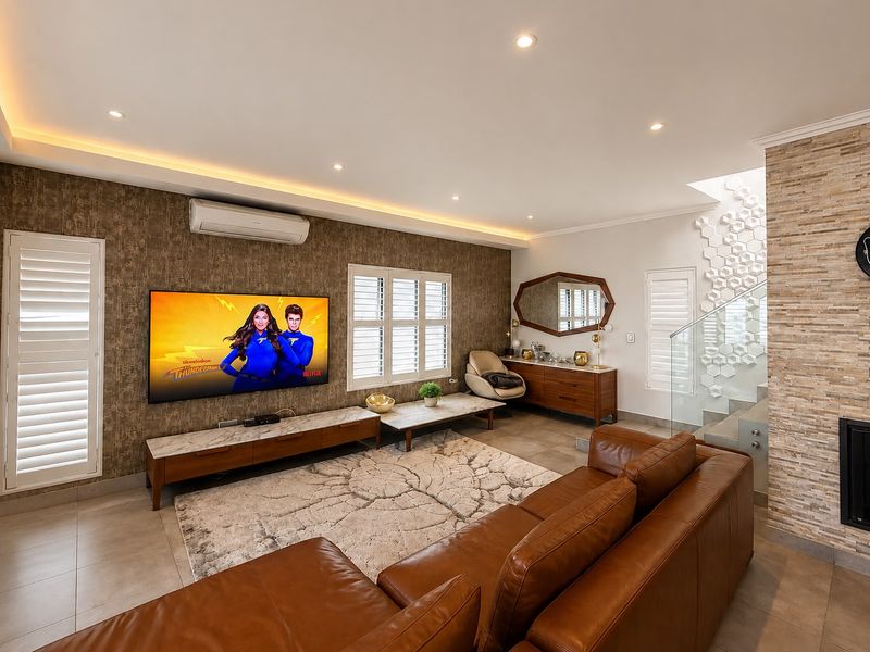 Modern living room featuring a stone-clad feature wall, recessed cove lighting, plantation shutters, and a glass balustrade staircase.