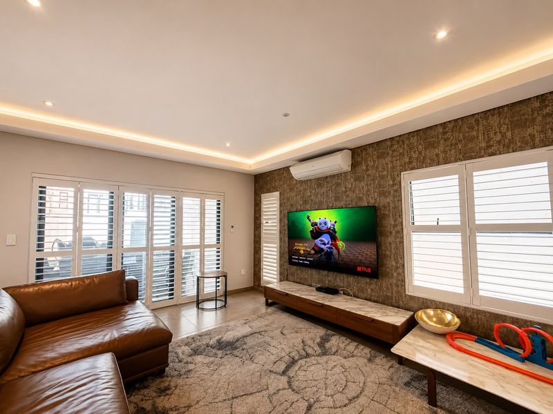 Modern living room featuring a textured feature wall, recessed cove lighting, split-system air conditioning, and plantation shutters on the windows.