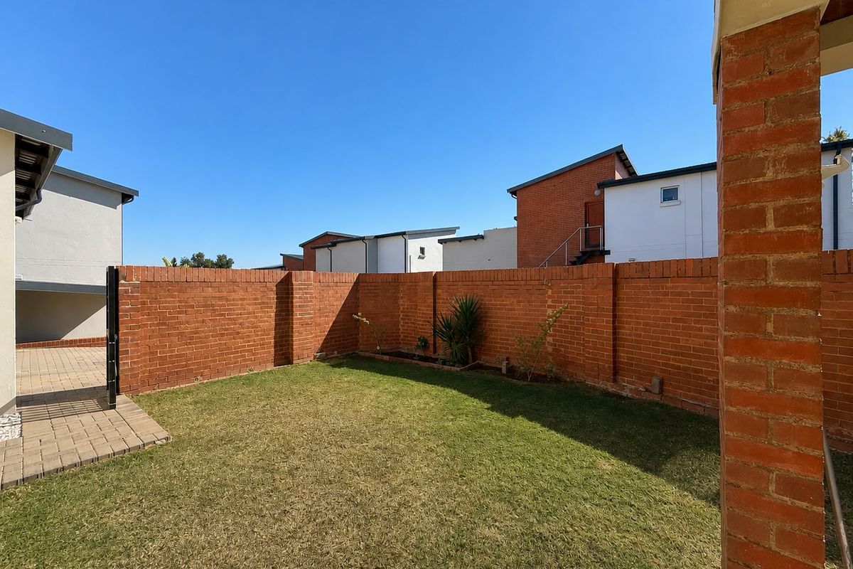 A private rear garden area featuring a well-maintained lawn, paved walkway, and secure brick boundary walling within a townhouse complex.