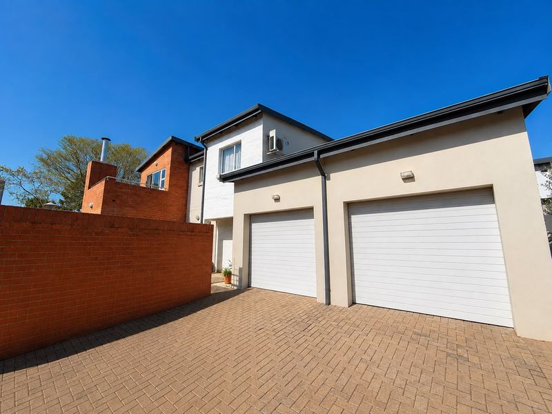 Front elevation of a townhouse featuring a double garage with automated doors, paved driveway, and a combination of brick and rendered exterior finishes.