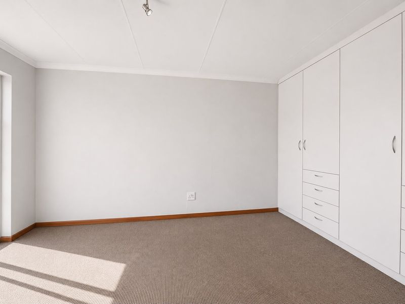 A clean, empty bedroom featuring neutral walls, carpeted flooring, and ample built-in cupboard storage.