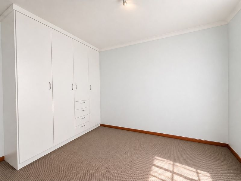 A clean, empty bedroom featuring neutral walls, carpeted flooring, and ample built-in cupboard storage.