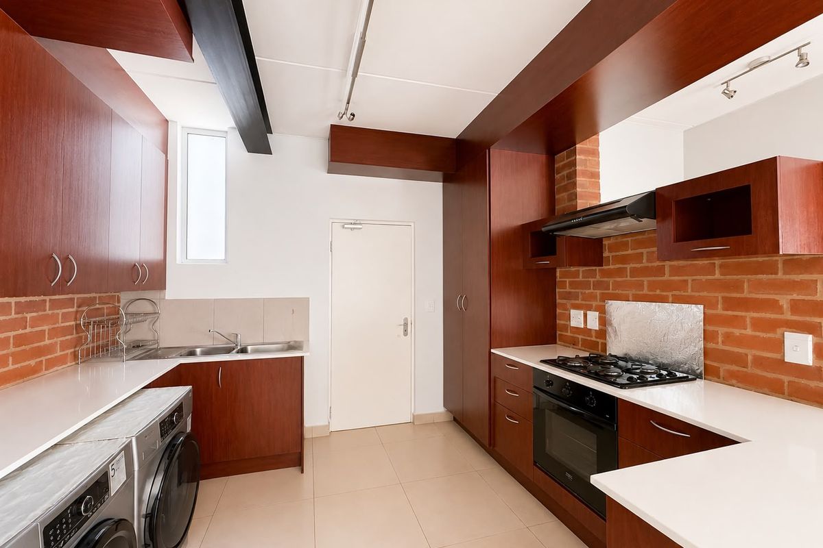 Modern kitchen featuring dark wood cabinetry, stone countertops, exposed brick accents, and integrated appliances including a gas hob and oven.