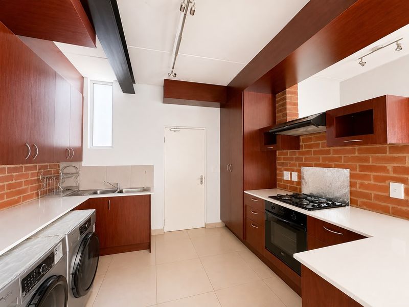 Modern kitchen featuring dark wood cabinetry, stone countertops, exposed brick accents, and integrated appliances including a gas hob and oven.