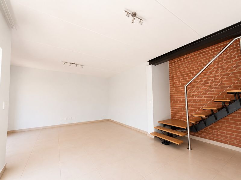 Spacious open-plan living area featuring modern tiled floors, an industrial-style steel staircase with wooden treads, and an exposed brick feature wall.