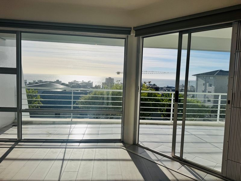 Bright and spacious living area featuring expansive floor-to-ceiling sliding glass doors that open onto a balcony with panoramic coastal and city views.