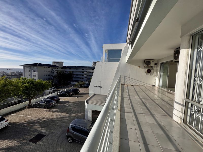 Spacious covered balcony with tiled flooring, metal balustrade, and sliding glass door access, offering an elevated view of the complex parking area.