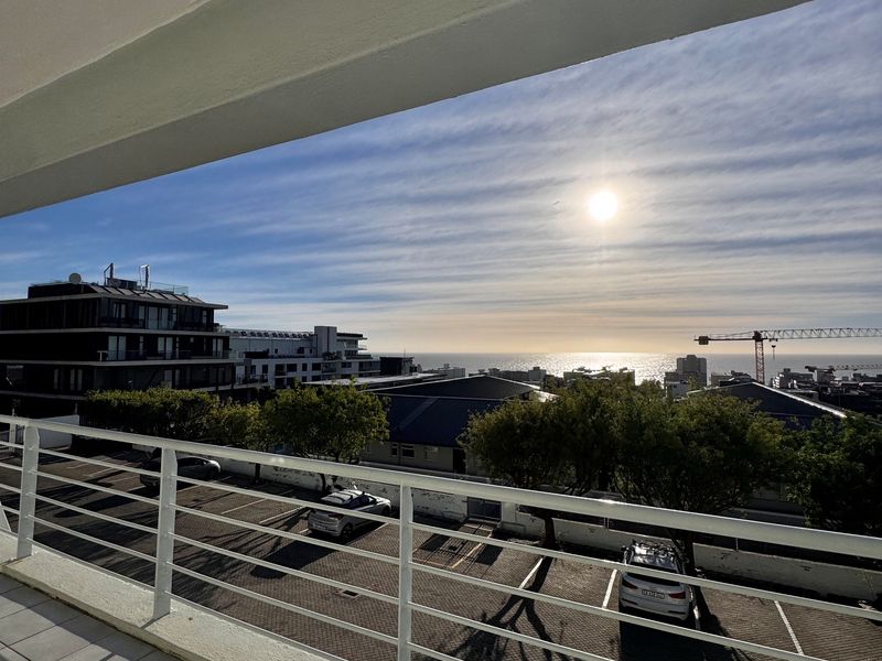 A spacious balcony featuring tiled flooring and a metal balustrade, offering an elevated view of the surrounding urban landscape and distant ocean.