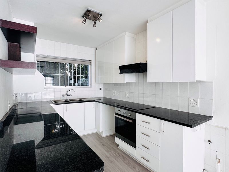 Modern kitchen featuring white cabinetry, black granite countertops, built-in oven, electric hob, and laminate flooring, offering a clean and functional workspace.