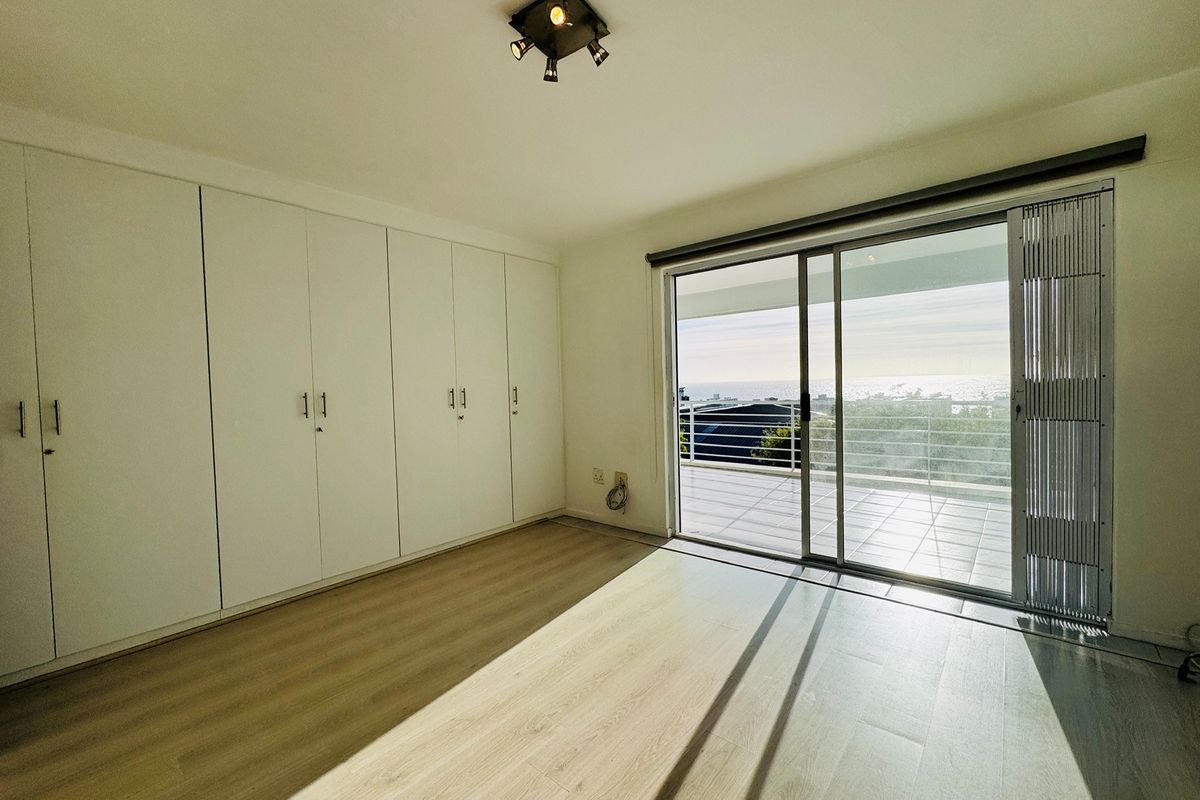 Bright bedroom featuring extensive built-in cupboards, light laminate flooring, and a sliding glass door leading to a balcony with ocean views.