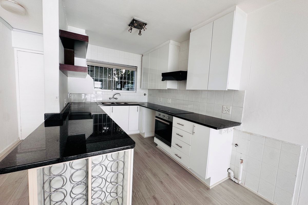 Modern kitchen featuring black granite countertops, white cabinetry, built-in oven, extractor fan, and laminate flooring in a clean, open-plan layout.