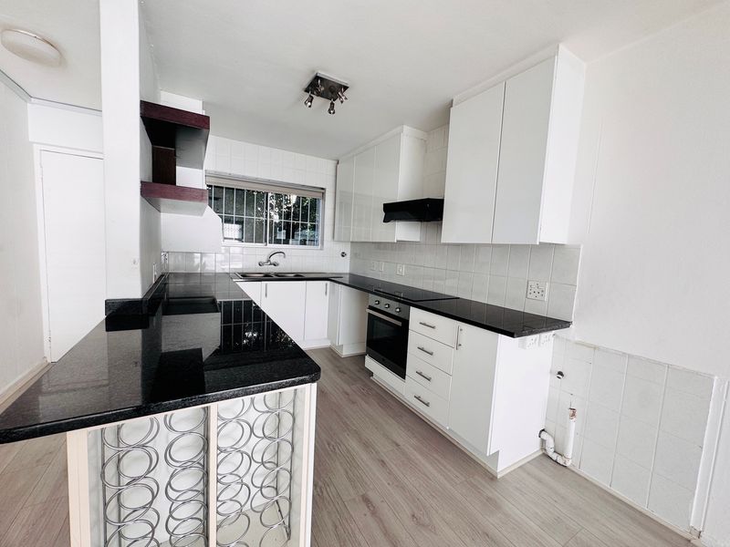 Modern kitchen featuring black granite countertops, white cabinetry, built-in oven, extractor fan, and laminate flooring in a clean, open-plan layout.