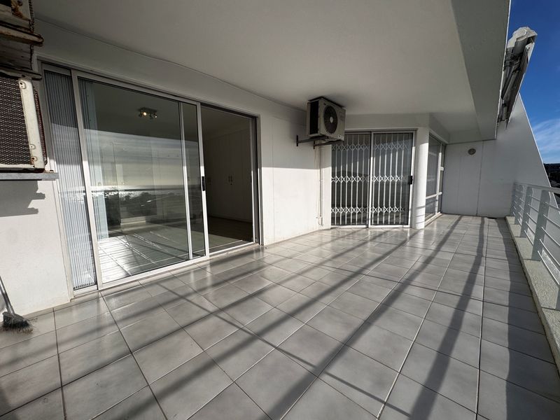 Spacious covered balcony featuring tiled flooring, sliding glass doors, and a metal railing, offering a functional outdoor space for the apartment.