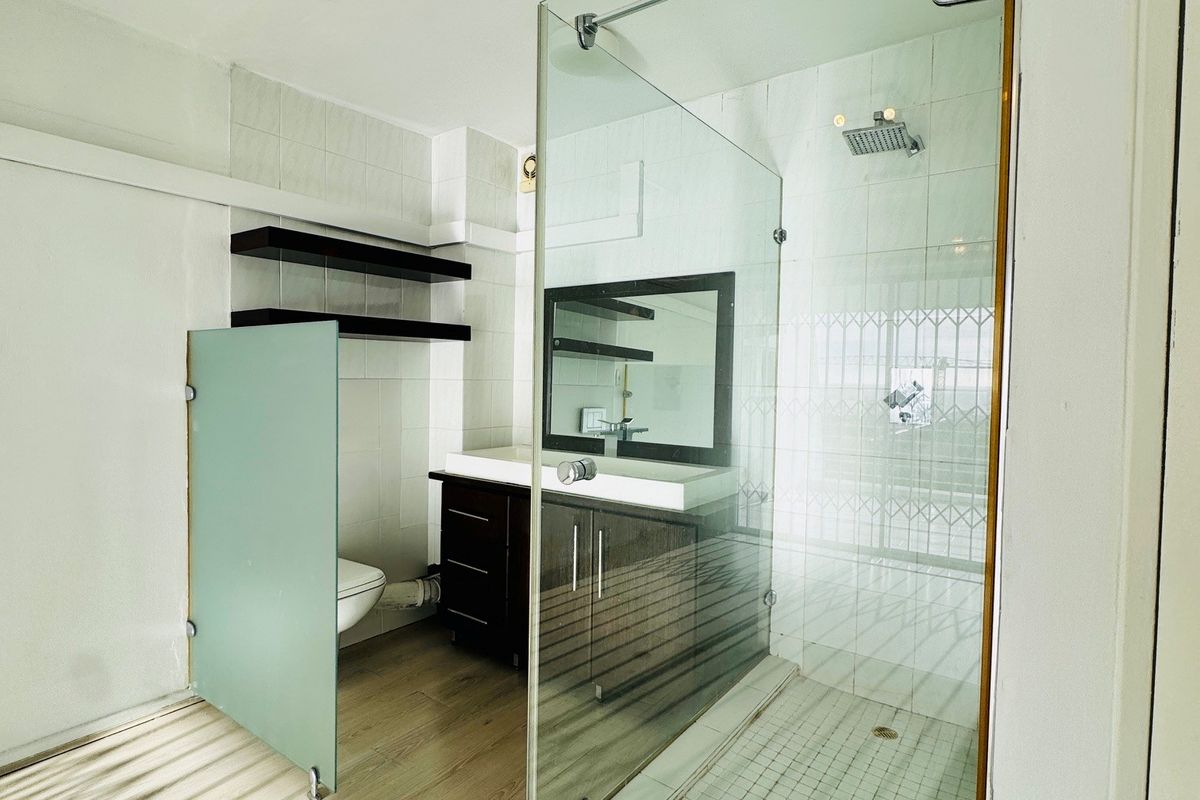 Modern bathroom featuring a glass-enclosed shower, vanity cabinet with mirror, and a frosted glass privacy screen for the toilet area.
