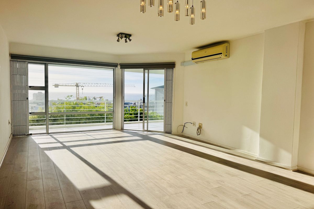 Spacious, light-filled living area featuring modern laminate flooring, split-system air conditioning, and large sliding doors opening to a balcony with scenic views.