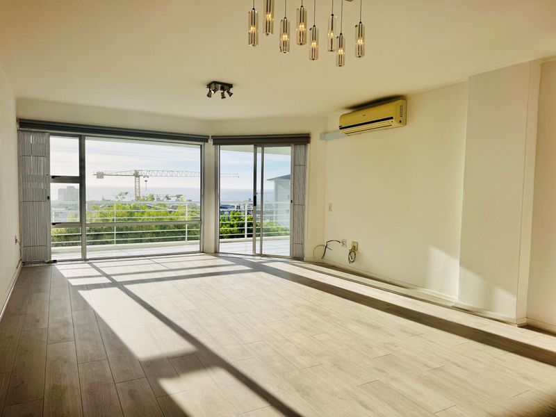 Spacious, light-filled living area featuring modern laminate flooring, split-system air conditioning, and large sliding doors opening to a balcony with scenic views.