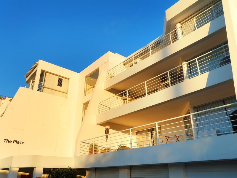 A modern apartment building facade featuring multiple levels of balconies with white metal railings and clear sliding glass doors.