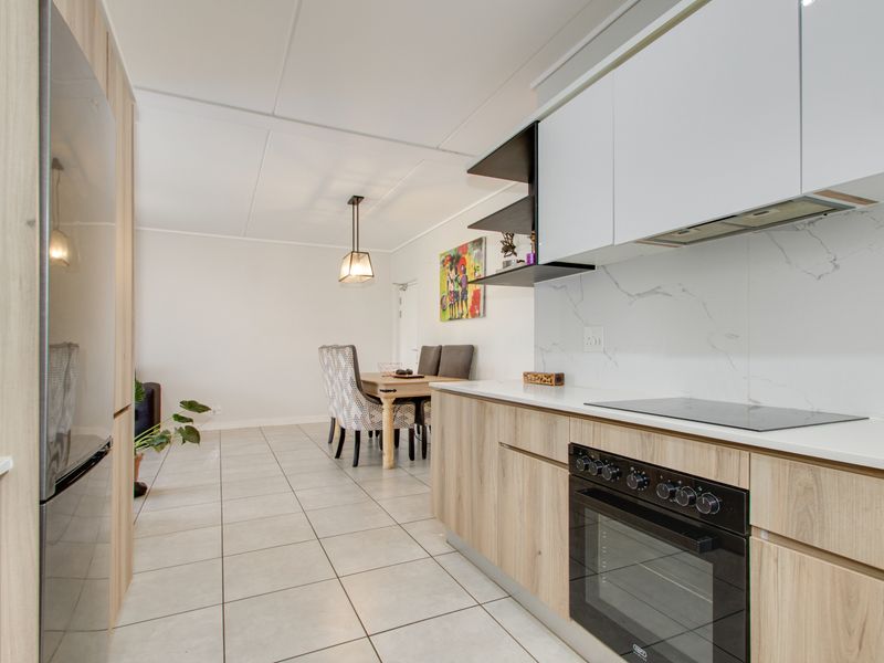 Modern open-plan kitchen and dining area featuring light wood cabinetry, marble-look splashback, integrated appliances, and neutral tiled flooring.