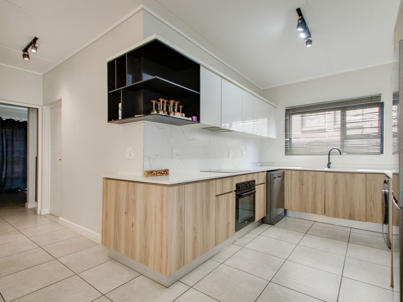 Modern kitchen featuring light wood-grain cabinetry, stone countertops, marble-look splashback, integrated appliances, and contemporary track lighting.