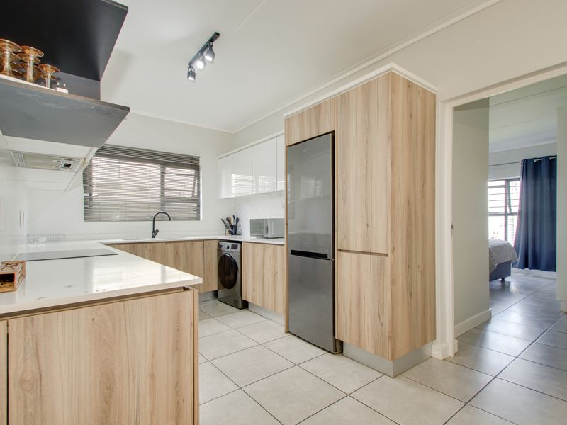 Modern kitchen featuring light wood-grain cabinetry, stone countertops, integrated appliances, tiled flooring, and contemporary track lighting.