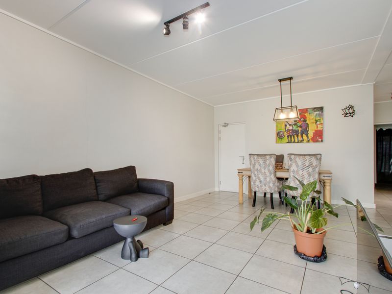 An open-plan living and dining area featuring neutral tiled flooring, modern track lighting, and a clean, minimalist aesthetic suitable for various interior styles.
