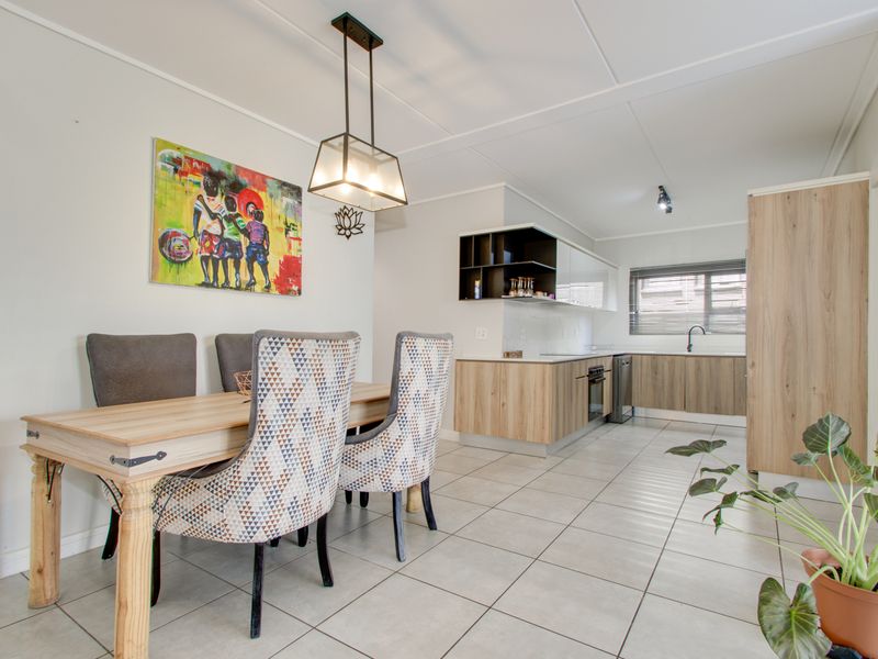 Modern open-plan living and dining area featuring tiled floors, contemporary wood-finish kitchen cabinetry, and integrated appliances, creating a bright and functional space.