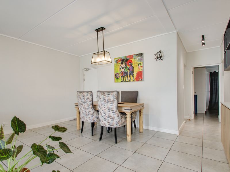 Open plan living and dining area featuring neutral tiled flooring, modern pendant lighting, and access to a functional kitchen space.