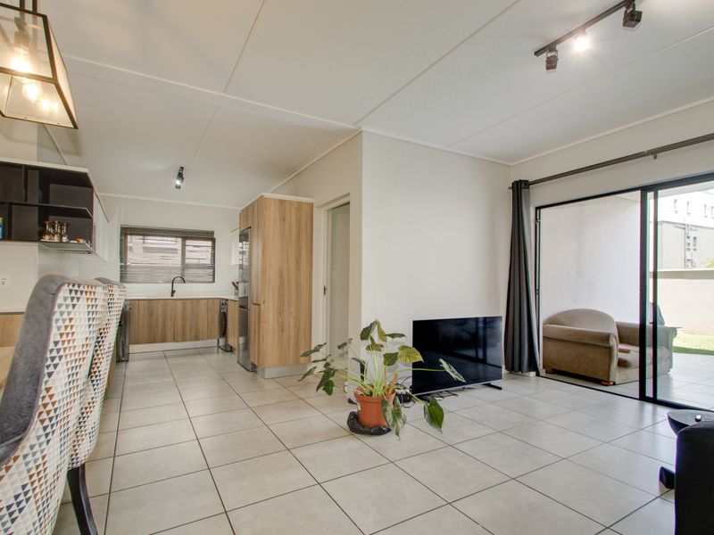 Modern open-plan living area featuring tiled floors, a contemporary kitchen with wood-finish cabinetry, and large sliding doors leading to an outdoor patio space.