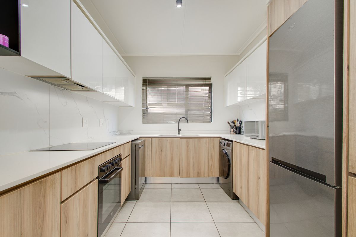 Modern galley-style kitchen featuring sleek white and wood-grain cabinetry, stone countertops, integrated appliances, and tiled flooring with a functional layout.