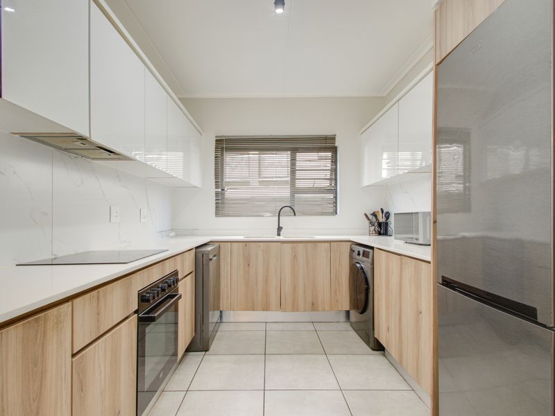 Modern galley-style kitchen featuring sleek white and wood-grain cabinetry, stone countertops, integrated appliances, and tiled flooring with a functional layout.
