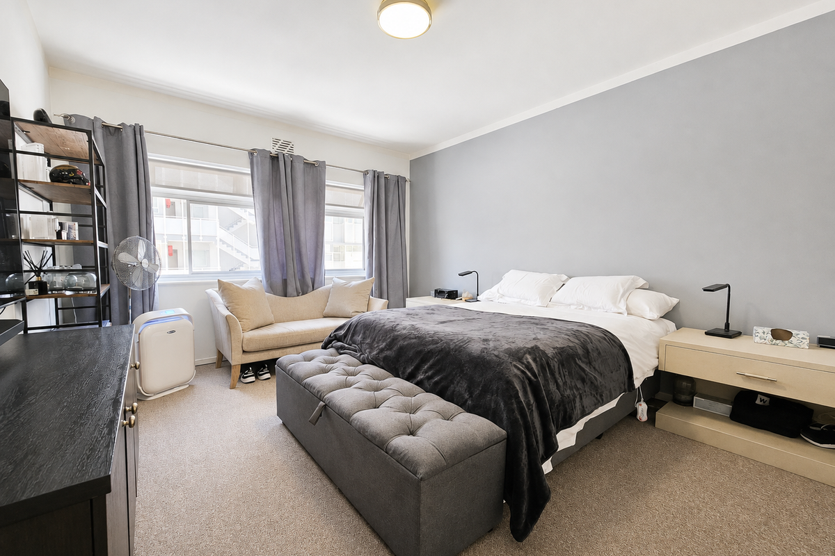 A well-maintained bedroom featuring neutral wall tones, carpeted flooring, and large sliding windows that provide natural light.