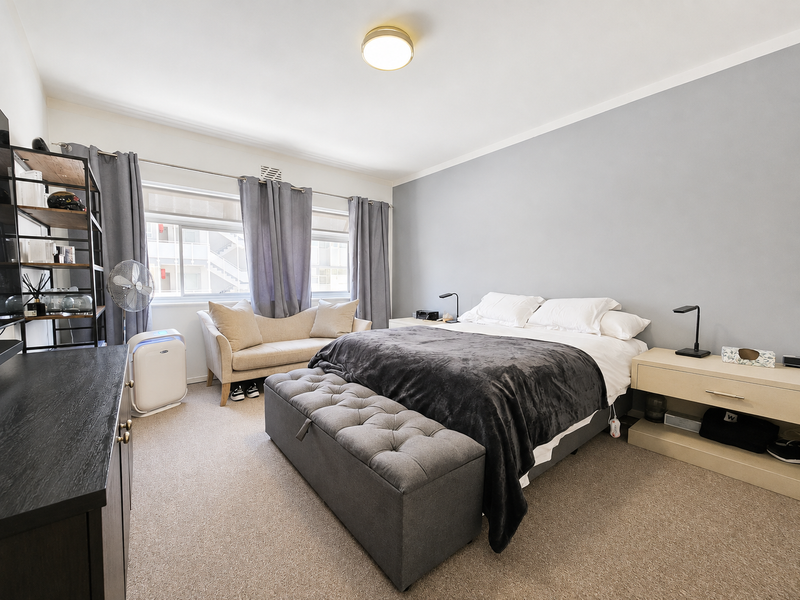 A well-maintained bedroom featuring neutral wall tones, carpeted flooring, and large sliding windows that provide natural light.