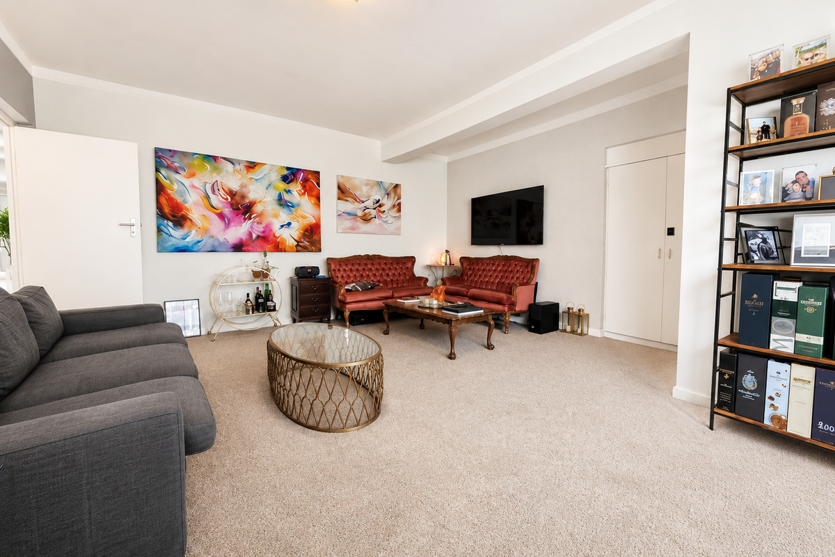 A spacious and well-maintained living room featuring neutral carpeting, a built-in storage cupboard, and ample space for comfortable seating arrangements.