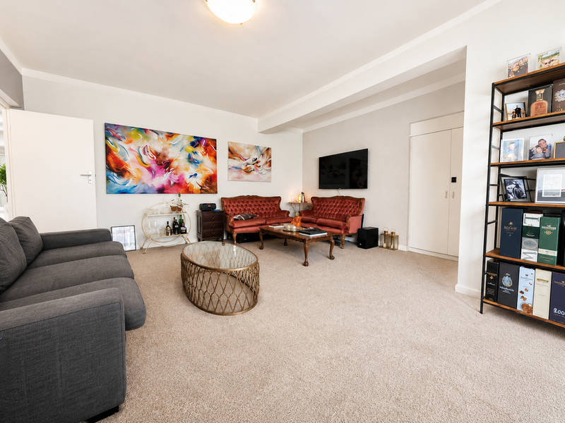 A spacious and well-maintained living room featuring neutral carpeting, a built-in storage cupboard, and ample space for comfortable seating arrangements.