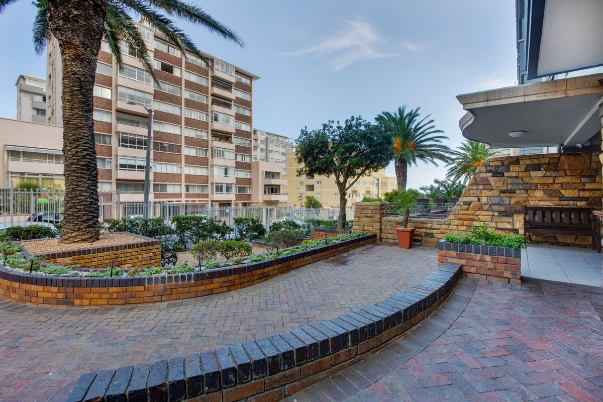 A well-maintained outdoor patio area featuring brick paving, stone-clad walls, and landscaped garden beds within an apartment complex setting.
