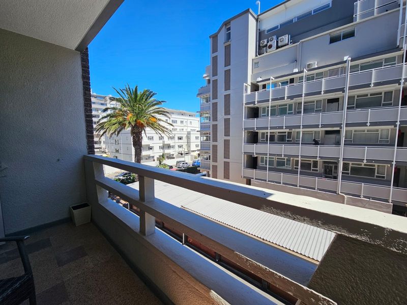 A clean, open-air balcony featuring tiled flooring and a sturdy railing, offering an urban view of the surrounding apartment complex.