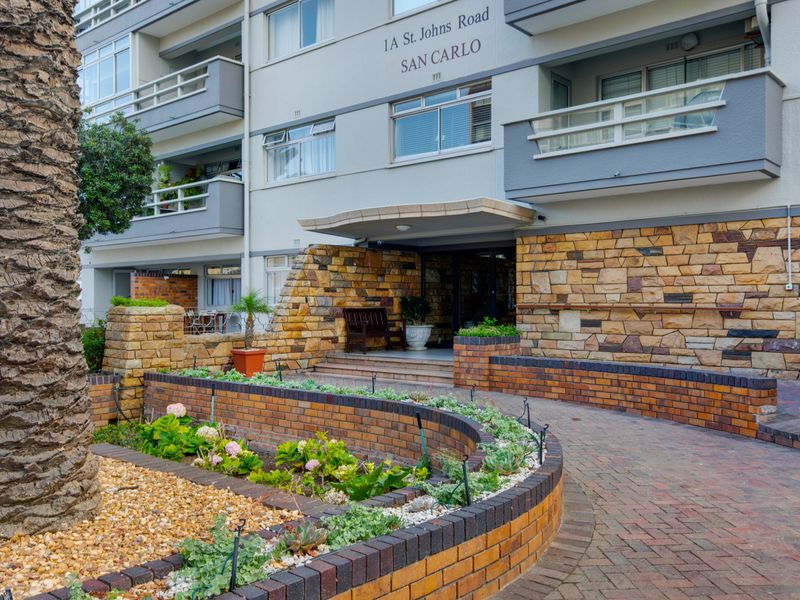 Front entrance of San Carlo apartment building featuring stone cladding, brick retaining walls, and a paved walkway leading to the main building access.