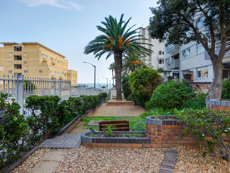 A well-maintained communal garden area featuring brick retaining walls, gravel pathways, mature palm trees, and secure metal perimeter fencing.