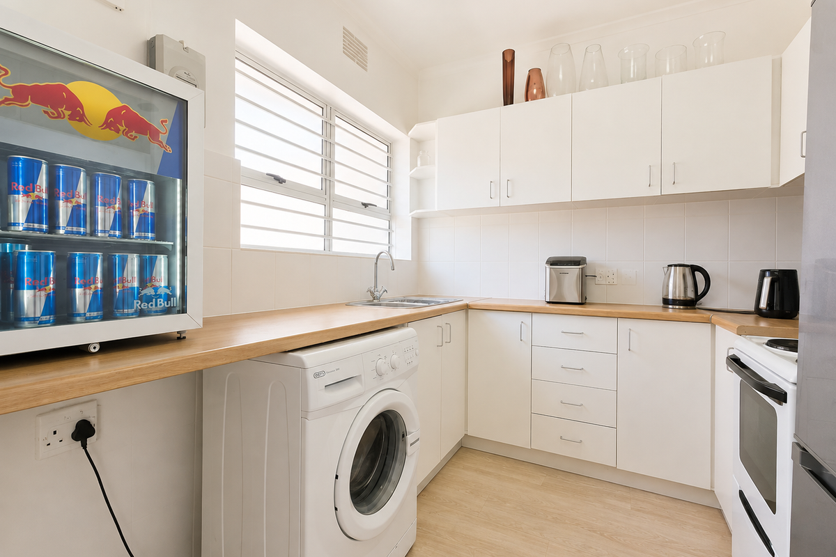 A functional kitchen featuring white cabinetry, laminate countertops, tiled splashbacks, and integrated laundry plumbing, complemented by a window with security bars.