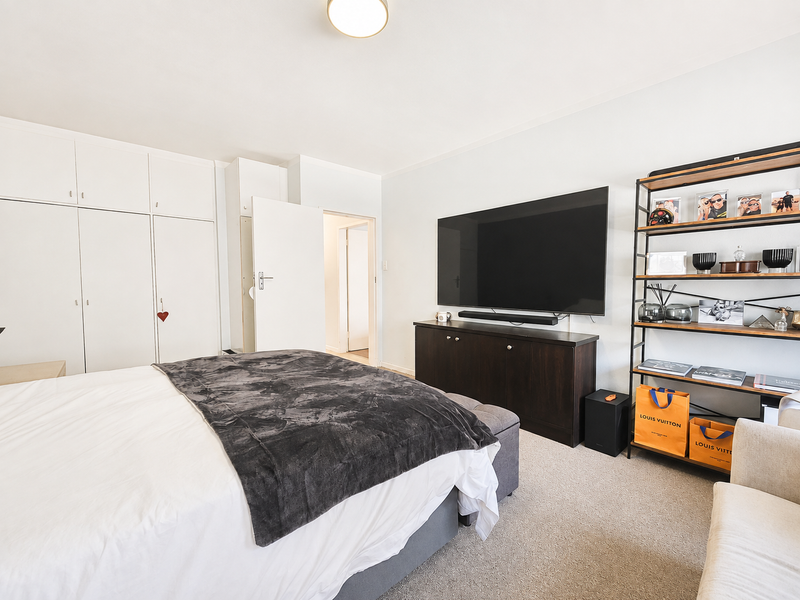 A well-maintained bedroom featuring neutral carpeted flooring, ample built-in cupboard storage, and a clean, bright interior layout.