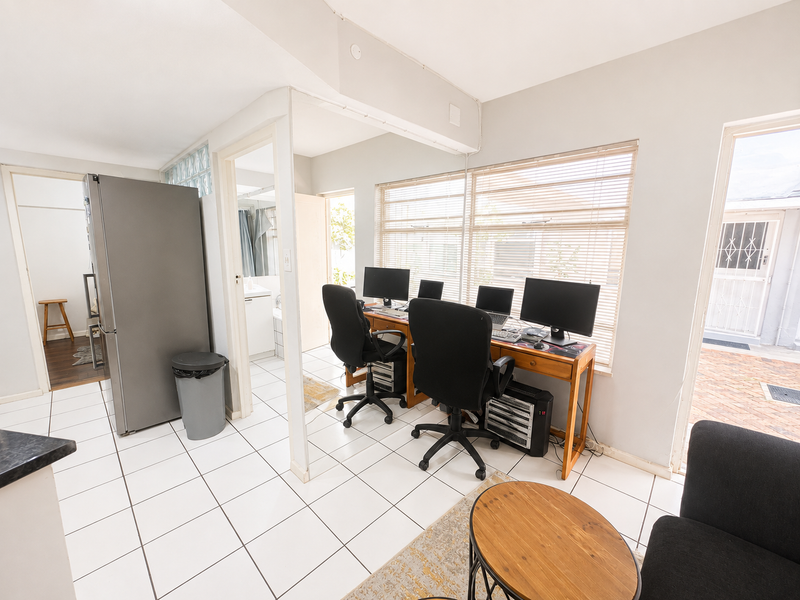 Open plan living area featuring tiled flooring, glass block accents, and large windows with venetian blinds, providing a functional workspace and access to the exterior.