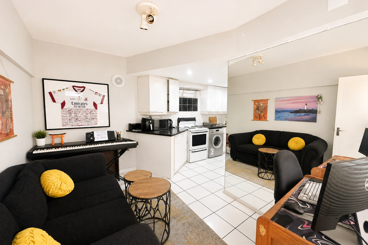 Open-plan living area featuring a compact kitchen with white cabinetry, tiled floors, and a large wall mirror reflecting the living space.