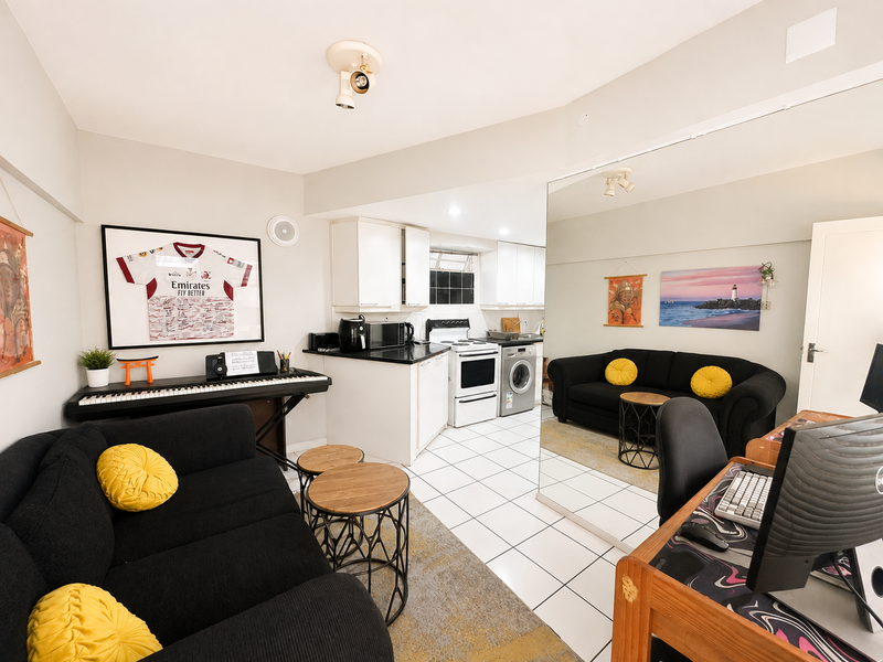 Open-plan living area featuring a compact kitchen with white cabinetry, tiled floors, and a large wall mirror reflecting the living space.