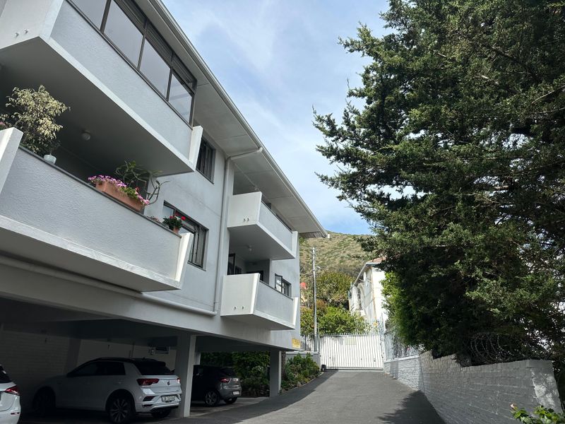 Exterior view of an apartment building featuring covered parking, private balconies, and a secure gated entrance.