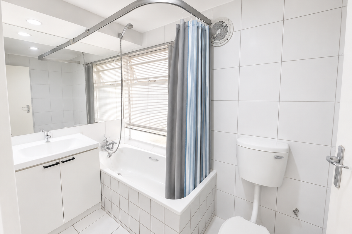 A clean, functional bathroom featuring a built-in vanity, bathtub with shower mixer, wall-mounted toilet, and full-height wall tiling.
